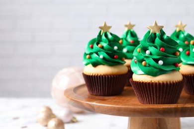 Photo of Christmas tree shaped cupcakes on wooden stand. Space for text