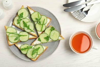 Photo of Plate with traditional English cucumber sandwiches and tea on white wooden table, flat lay