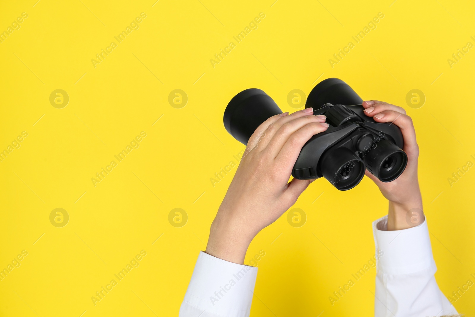 Photo of Woman holding modern binoculars on yellow background, closeup. Space for text