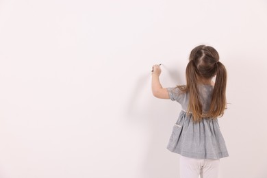 Photo of Little girl drawing on white wall indoors, back view. Space for text