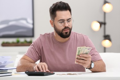 Young man counting money at white table indoors