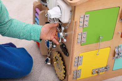 Photo of Little child playing with busy board house on floor, closeup
