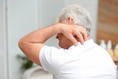 Photo of Senior man scratching neck indoors. Allergy symptom