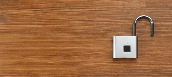 Photo of Modern padlock on wooden table, top view. Space for text