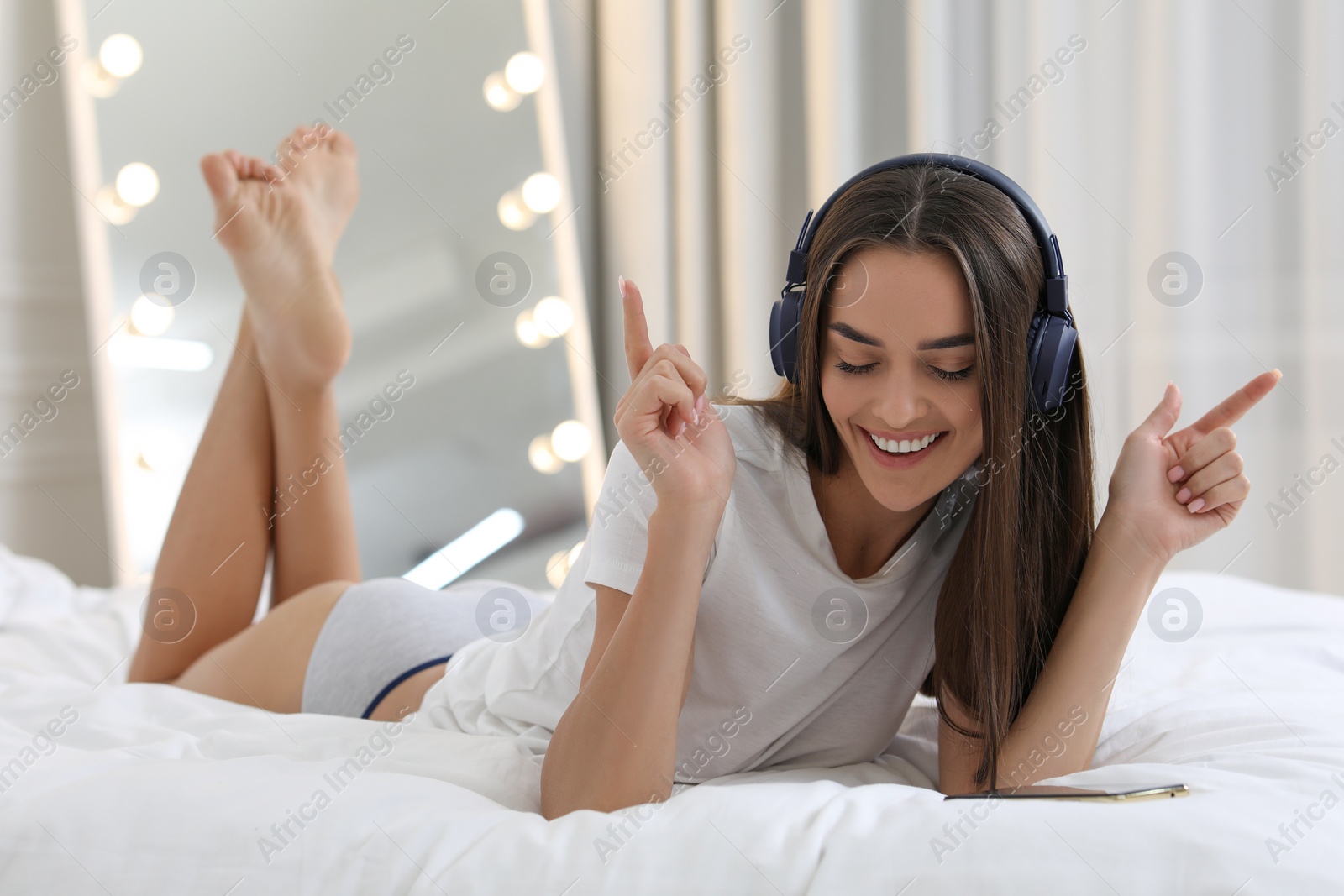 Photo of Young woman in white t-shirt and underwear listening to music on bed indoors