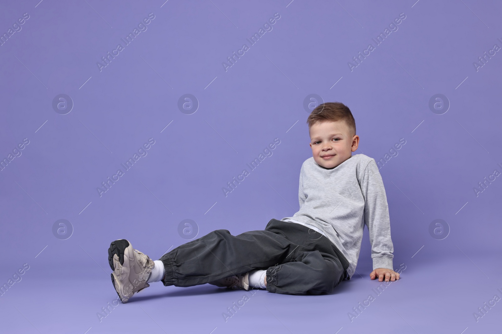 Photo of Happy little boy dancing on violet background