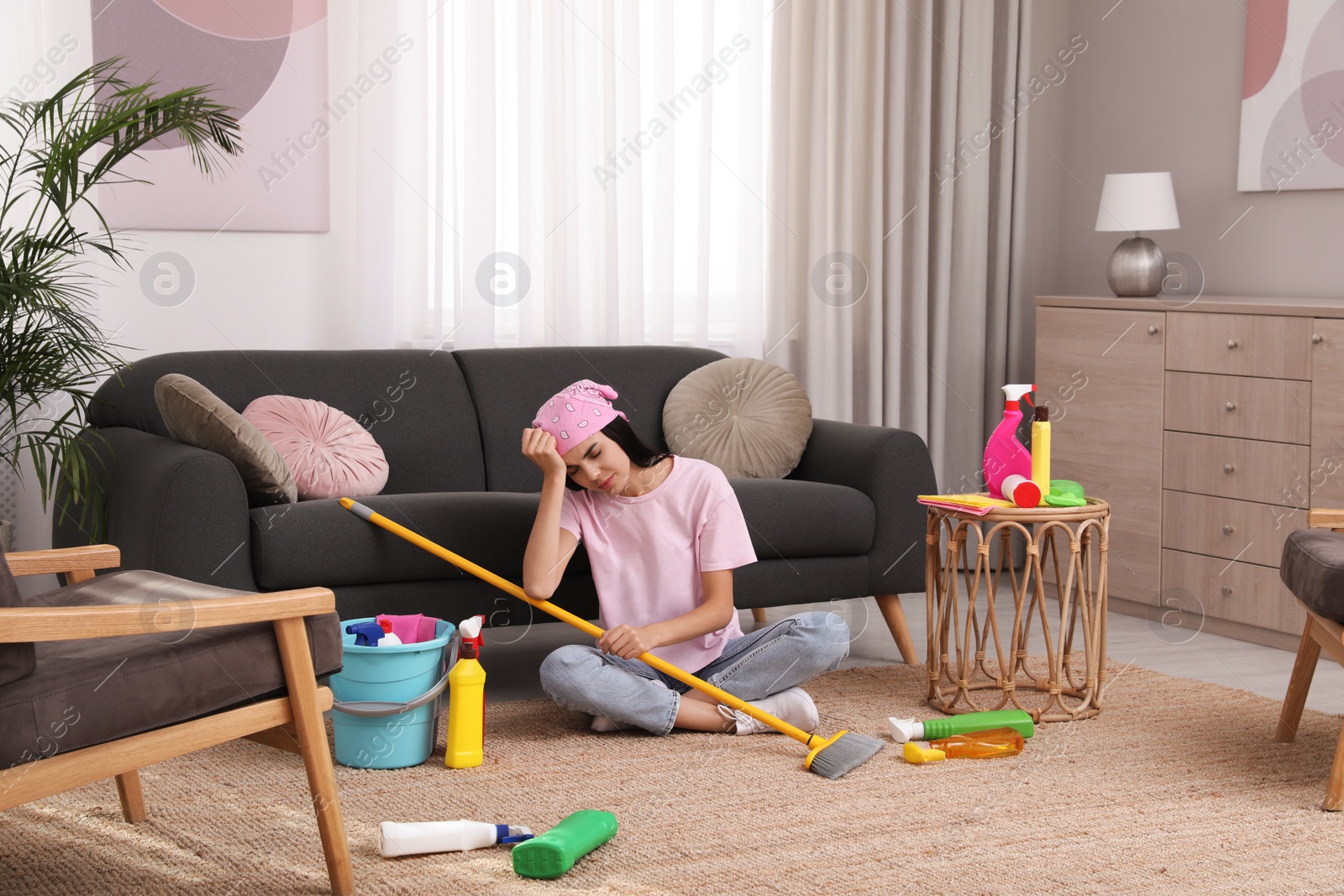 Photo of Tired young woman sitting on floor and cleaning supplies in living room