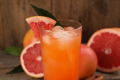 Photo of Tasty grapefruit drink with ice, slice of fruit and leaf in glass on table, closeup