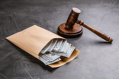 Dollar bills in envelope and gavel on grey stone table. Bribe concept