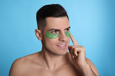 Photo of Man applying green under eye patch on light blue background