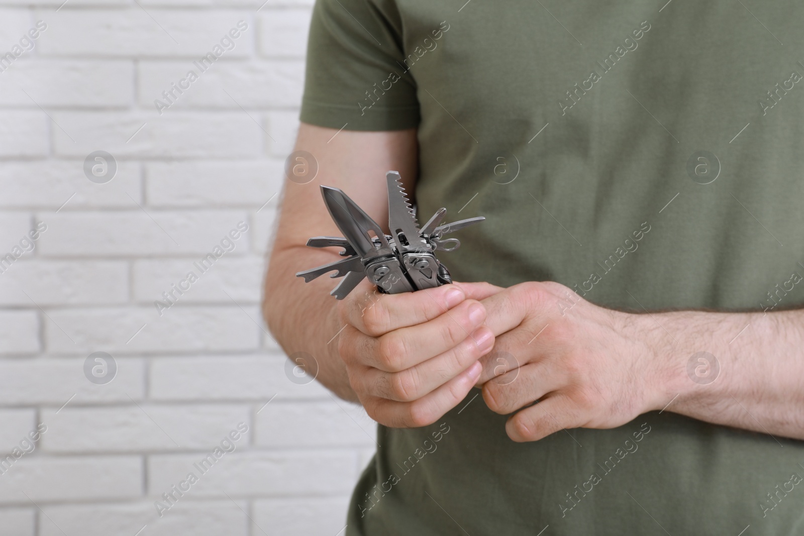 Photo of Man holding multitool near white brick wall, closeup