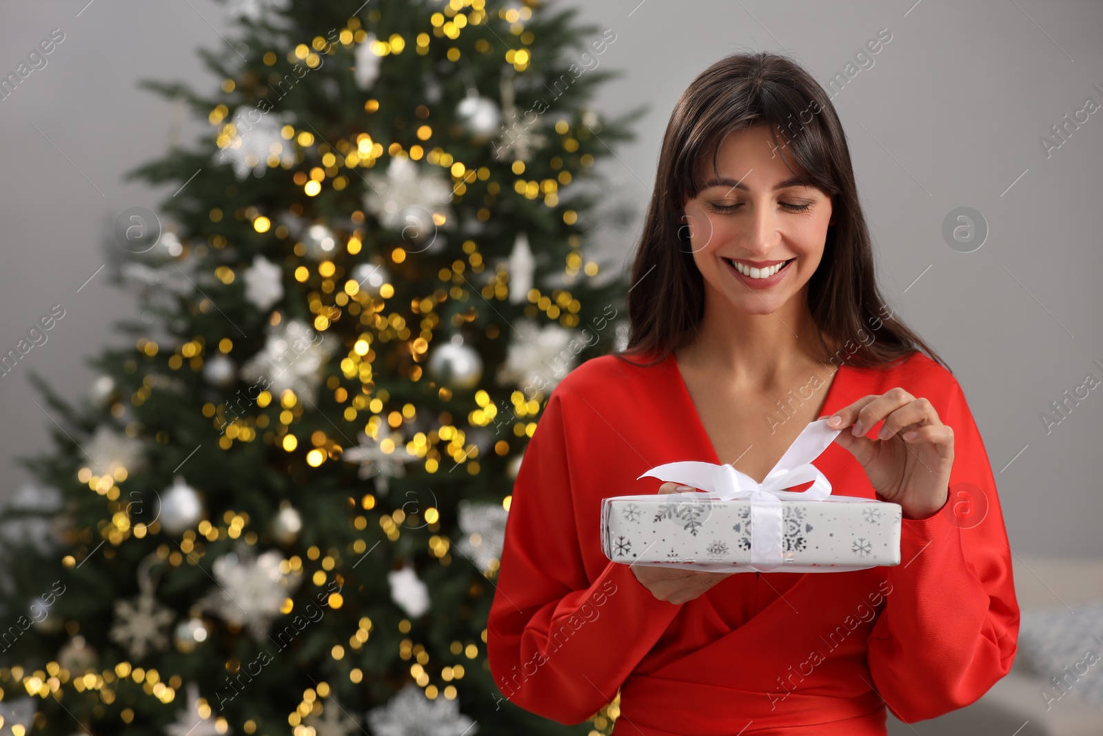 Photo of Smiling woman opening Christmas gift at home. Space for text