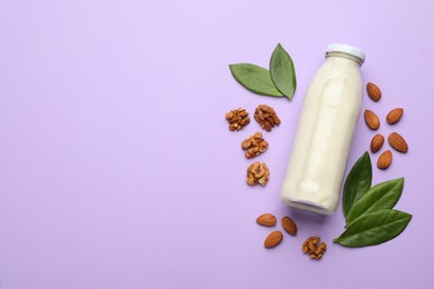 Photo of Bottle of vegan milk, walnuts and almonds on violet background, flat lay. Space for text