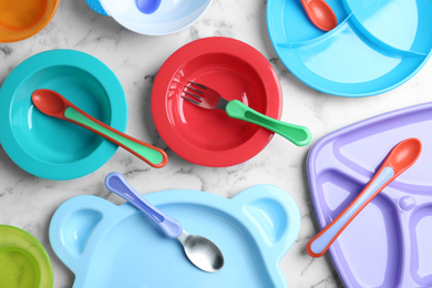 Photo of Set of colorful plastic dishware on white marble table, flat lay. Serving baby food