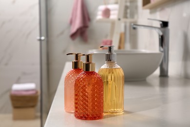 Photo of Glass dispensers with liquid soap on white table in bathroom