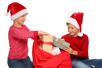 Photo of Cute little children in Santa hats pulling gift boxes out of red Christmas bag on white background