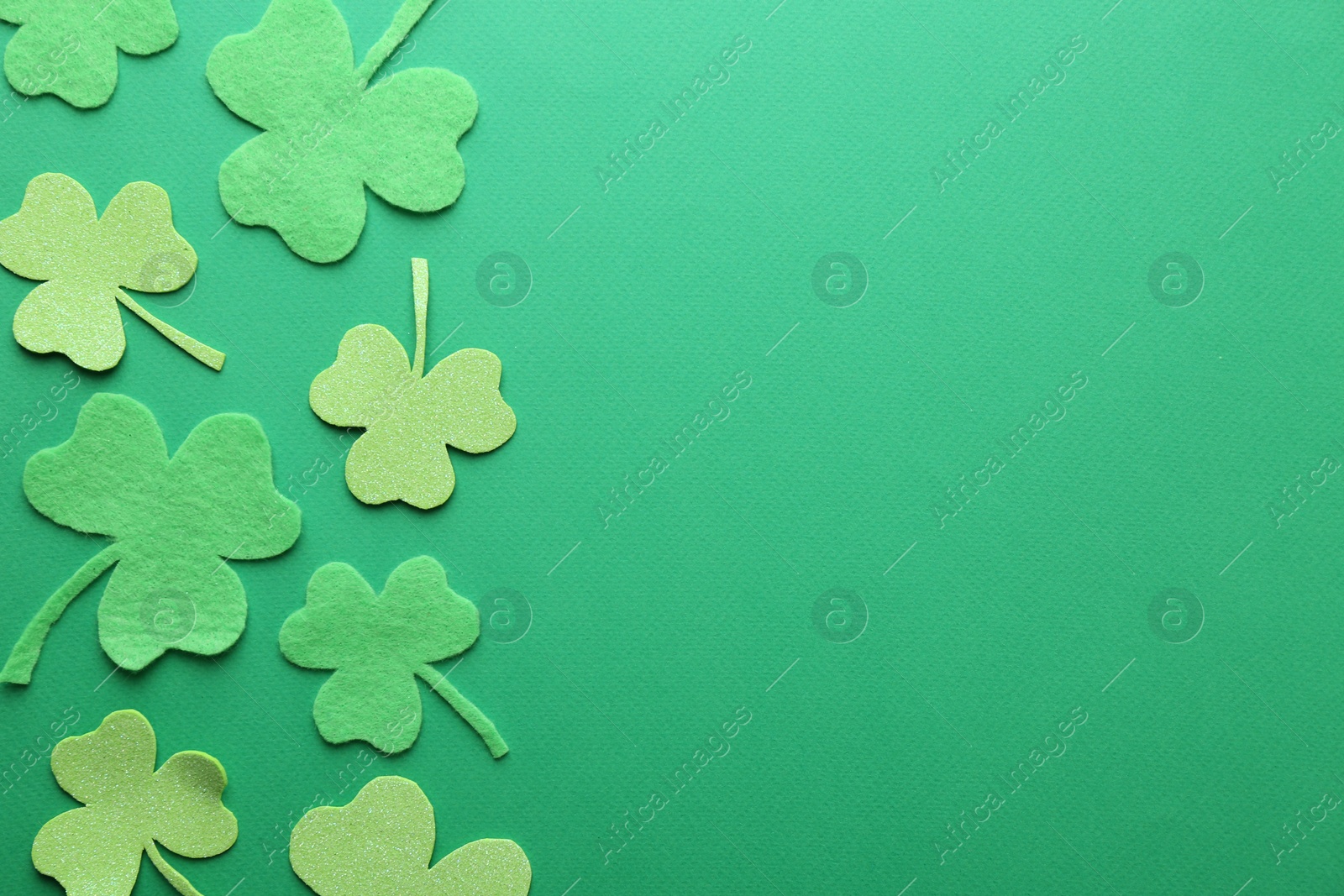 Photo of St. Patrick's day. Decorative clover leaves on green background, flat lay. Space for text