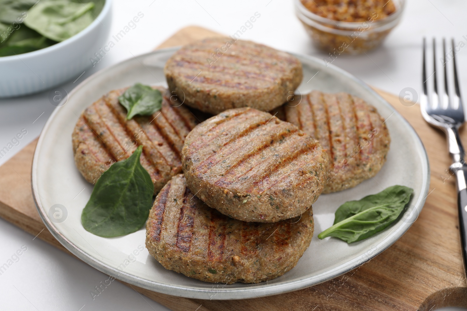 Photo of Tasty grilled vegan cutlets and spinach on white table, closeup