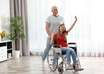 Happy grandfather and teenage girl in wheelchair at home