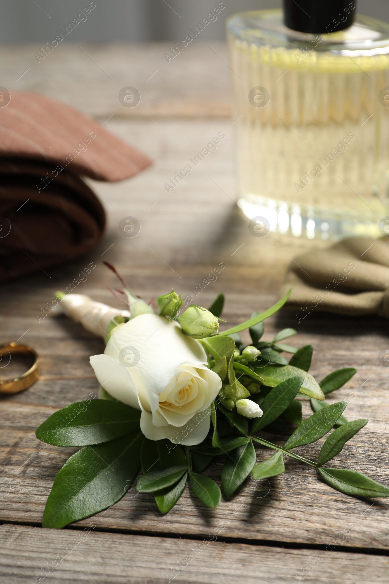 Photo of Wedding stuff. Stylish boutonniere, perfume and ring on wooden table, closeup