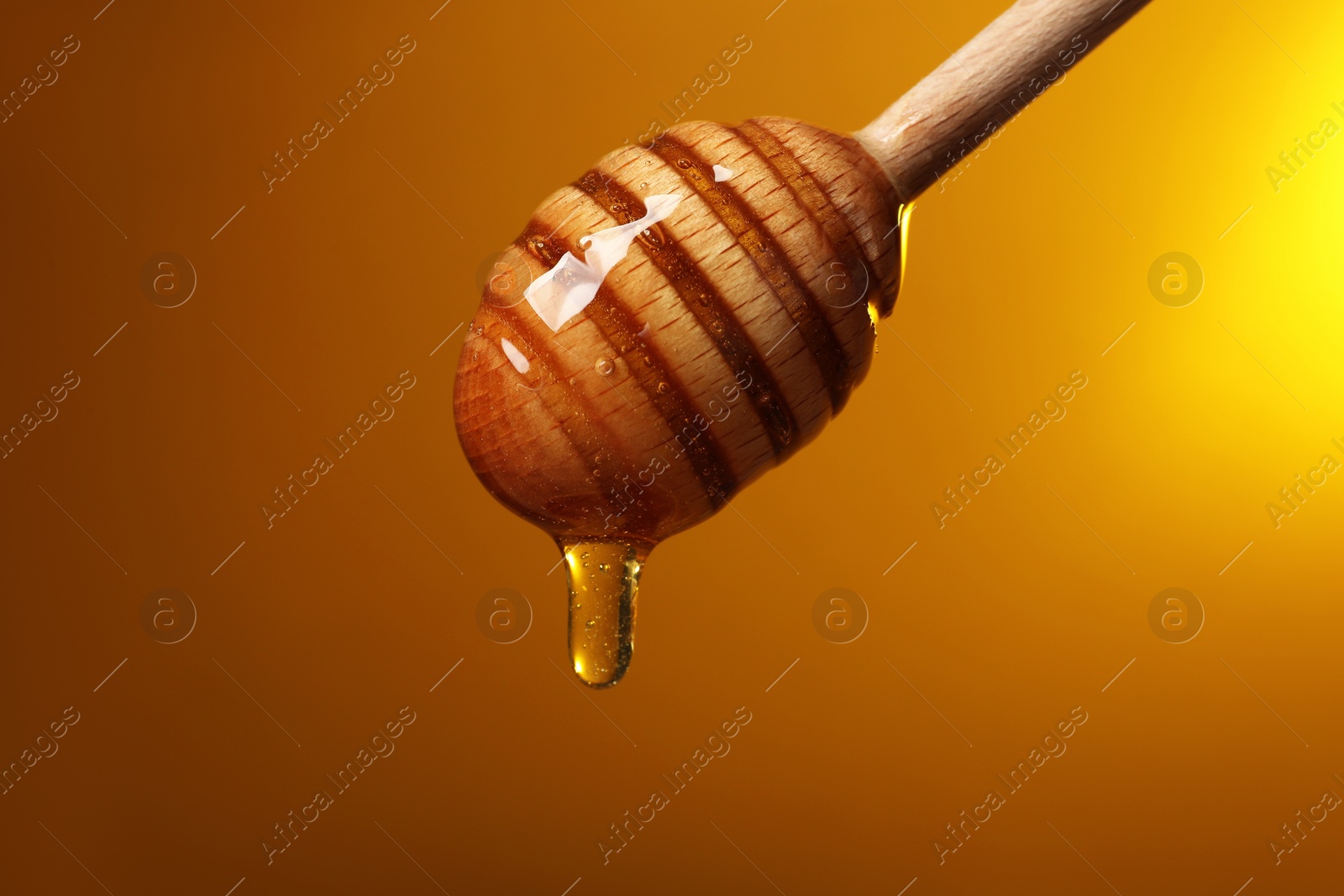 Photo of Pouring honey from dipper against golden background