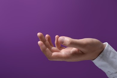 Man holding something in hand on purple background, closeup. Space for text
