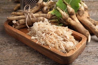 Photo of Grated horseradish and roots on wooden table, closeup
