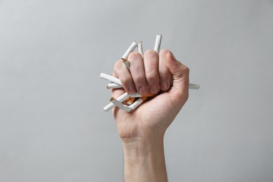 Photo of Stop smoking. Man holding broken cigarettes on grey background, closeup
