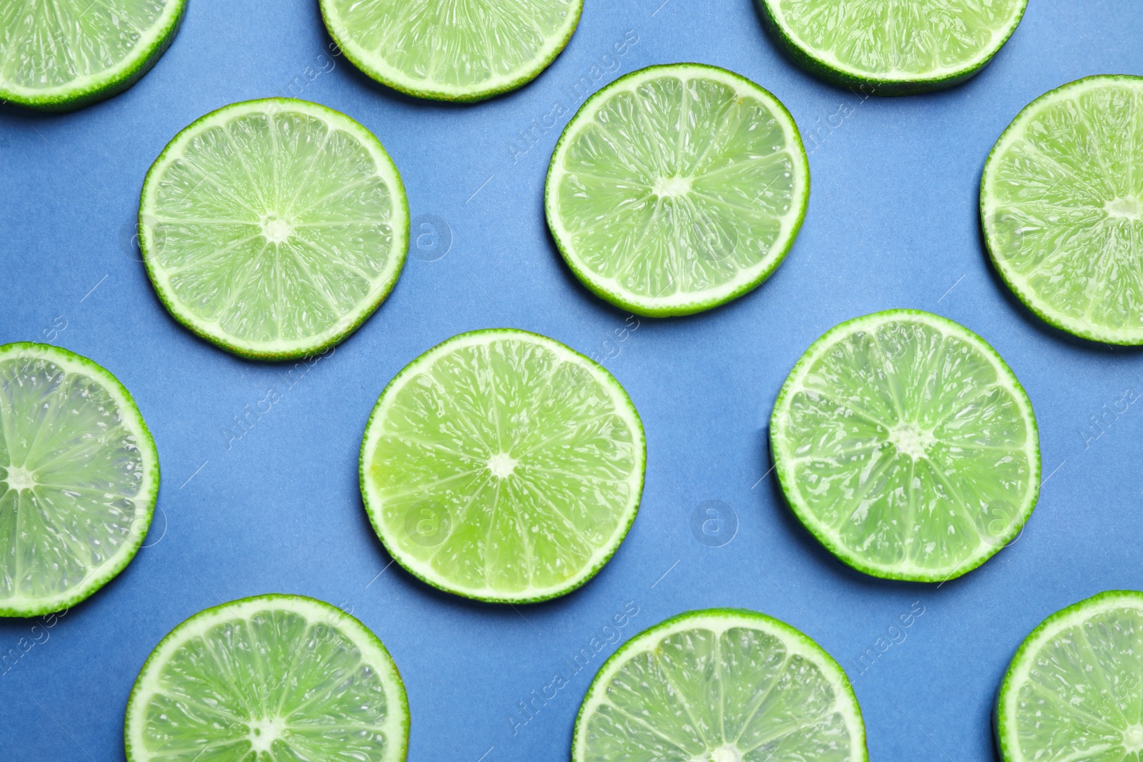 Photo of Juicy fresh lime slices on blue background, flat lay