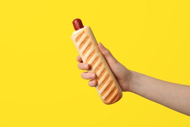 Photo of Woman holding delicious french hot dog on yellow background, closeup