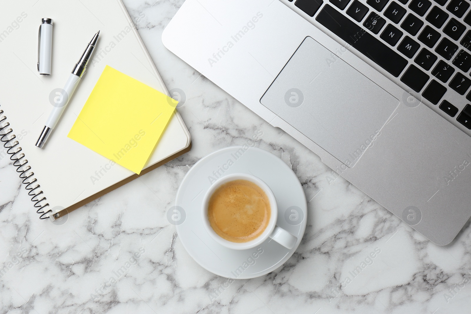 Photo of Notebook with blank sticky note, laptop and cup of coffee on white marble table, flat lay