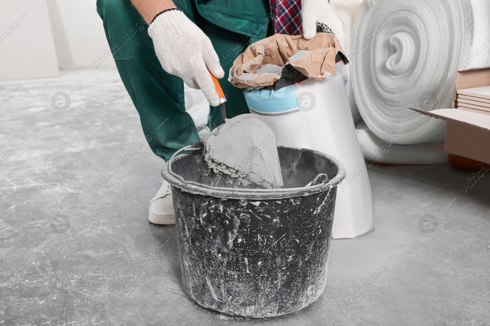 Photo of Worker with cement powder and trowel mixing concrete in bucket indoors, closeup