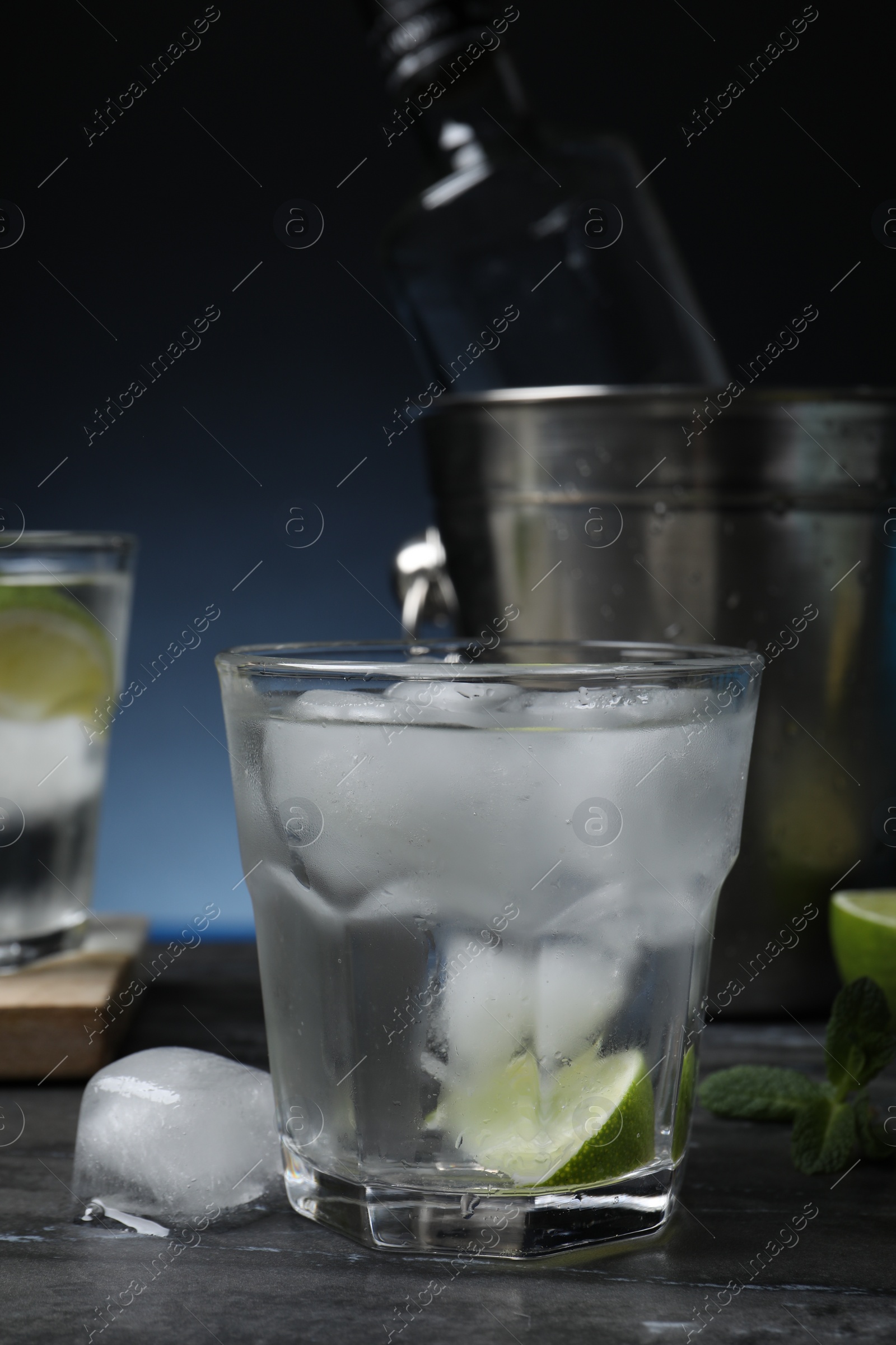 Photo of Glass of vodka with lime and ice on black marble table