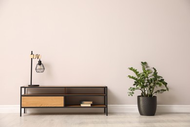 Photo of Elegant room interior with wooden cabinet, lamp and houseplant near light wall