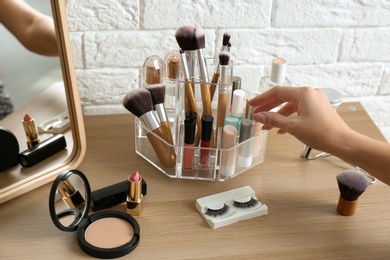 Photo of Woman taking cosmetics from organizer for makeup products on table