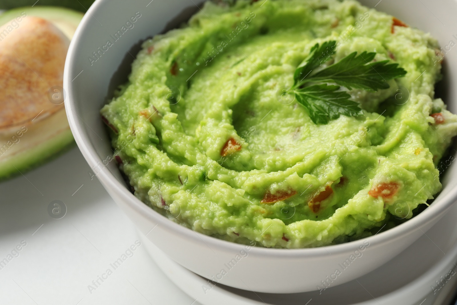 Photo of Bowl of delicious guacamole with parsley on white table, closeup