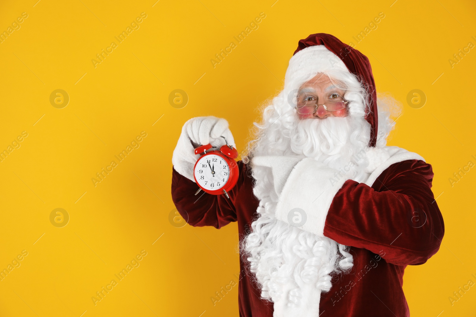 Photo of Santa Claus holding alarm clock on yellow background, space for text. Christmas countdown