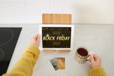 Photo of Woman using tablet with Black Friday announcement at kitchen counter, closeup
