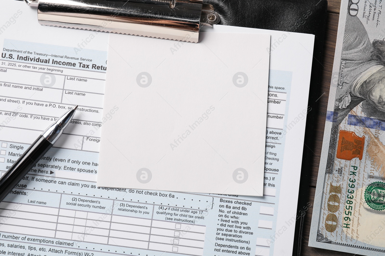 Photo of Tax return form, paper note, dollar banknotes and pen on table, top view