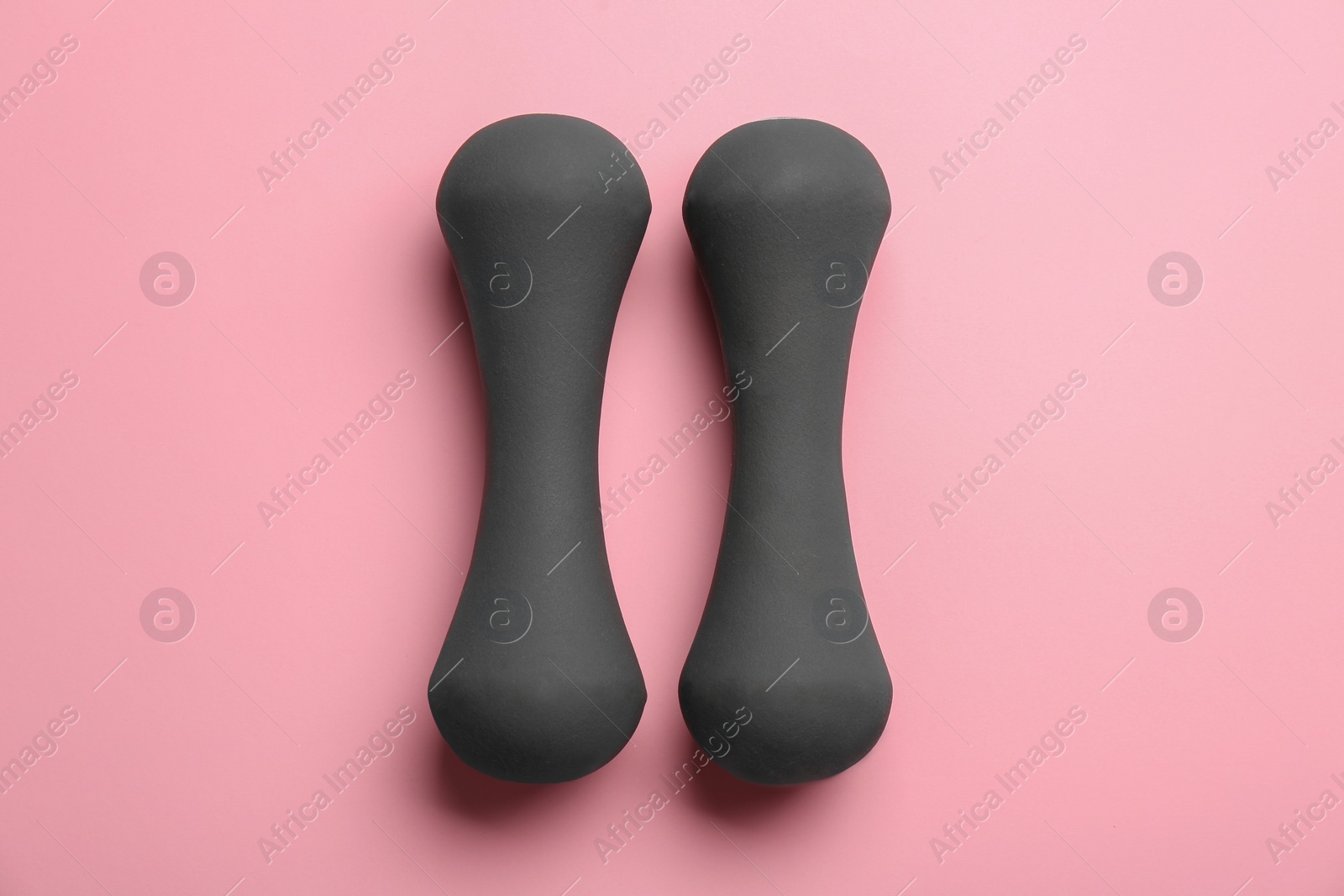 Photo of Grey dumbbells on pink background, flat lay