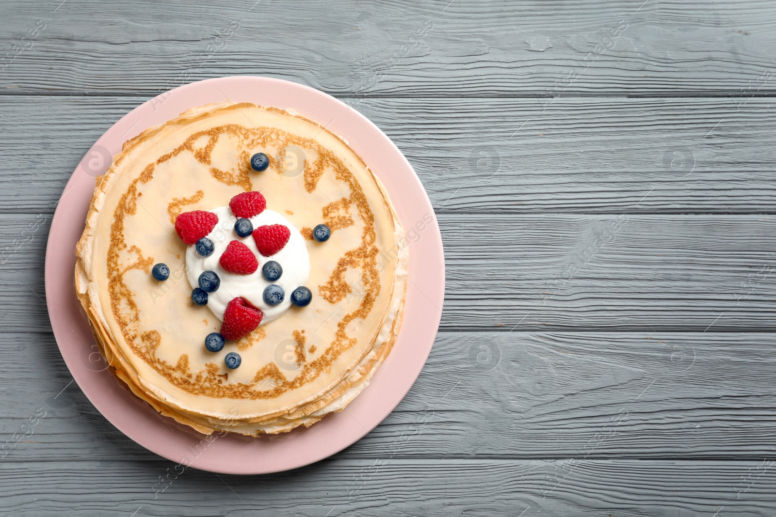 Photo of Thin pancakes served with cream and berries on plate, top view