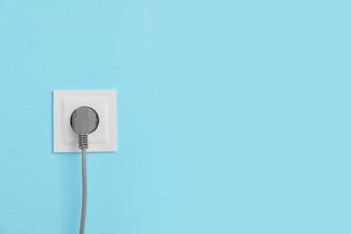 Photo of Power socket with inserted plug on light blue wall, space for text. Electrical supply