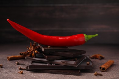 Photo of Delicious chocolate, fresh red chili pepper and spices on grey textured table