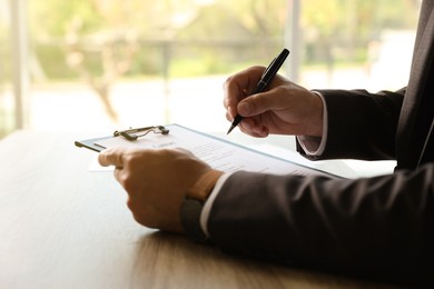 Photo of Businessman signing document at table indoors, closeup