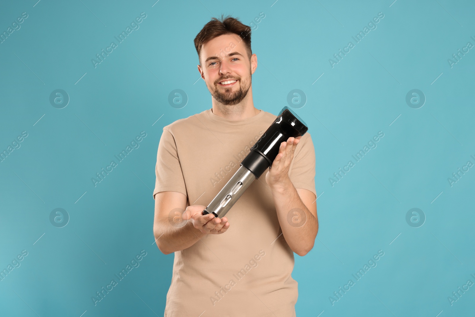 Photo of Smiling man holding sous vide cooker on light blue background