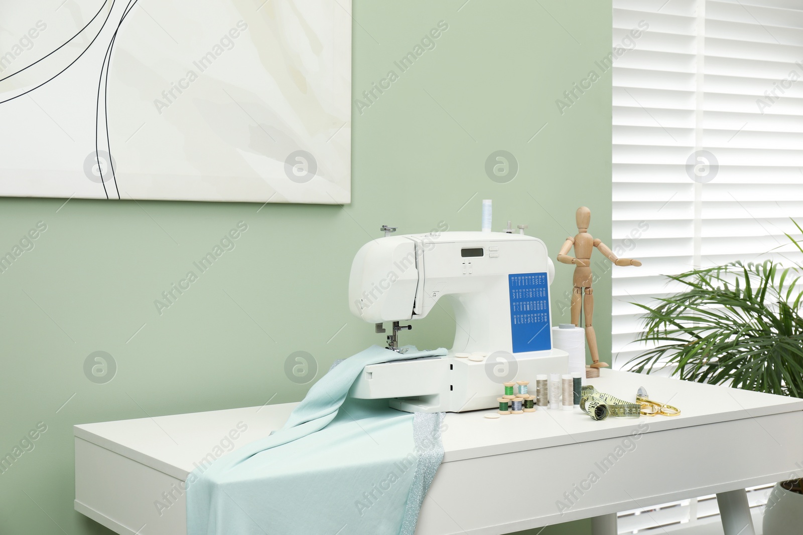 Photo of Modern sewing machine with cloth and craft accessories on white table near window in room