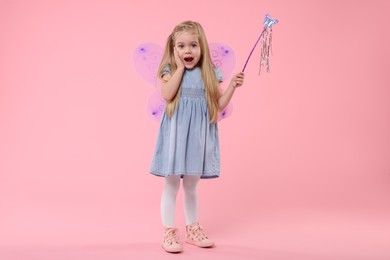 Photo of Surprised little girl in fairy costume with violet wings and magic wand on pink background