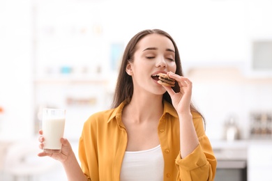 Beautiful young woman drinking milk with cookies at home