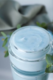 Photo of Jar of organic cream and eucalyptus on mirror surface, closeup