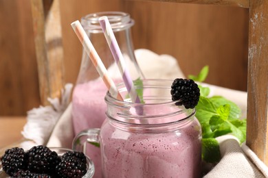 Photo of Different glassware of delicious blackberry smoothie and fresh berries on wooden background, closeup